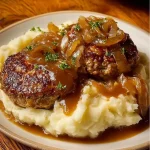 Nahaufnahme von einer Bulette auf Kartoffelbrei mit brauner Zwiebelsoße übergossen