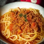 Ein großer Topf mit dampfender Bolognese-Soße neben einer Schüssel Spaghetti